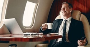 Picture of business man on a plane in front of a laptop and holding a coffee cup