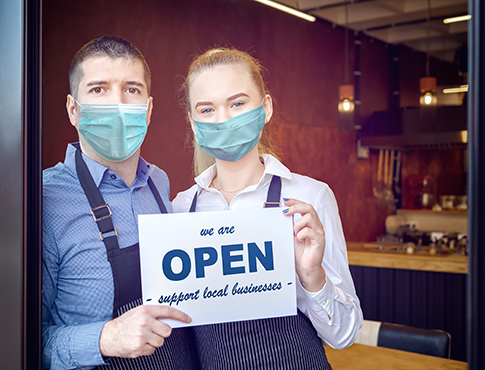 man and woman in aprons and masks working at a restaurant holding up a sign that says support small businesses.