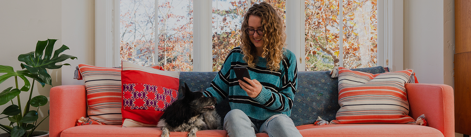 woman sitting on orange couch with dog looking at cell phone