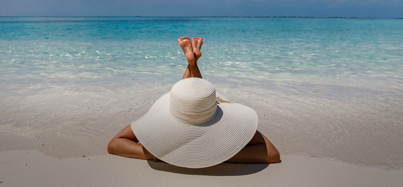 lady laying down on the sand by a beach wearing a big white hat