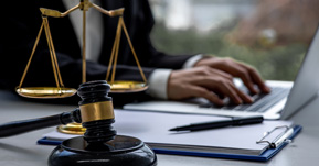 Man writing on laptop computer at a desk with scales and gavel