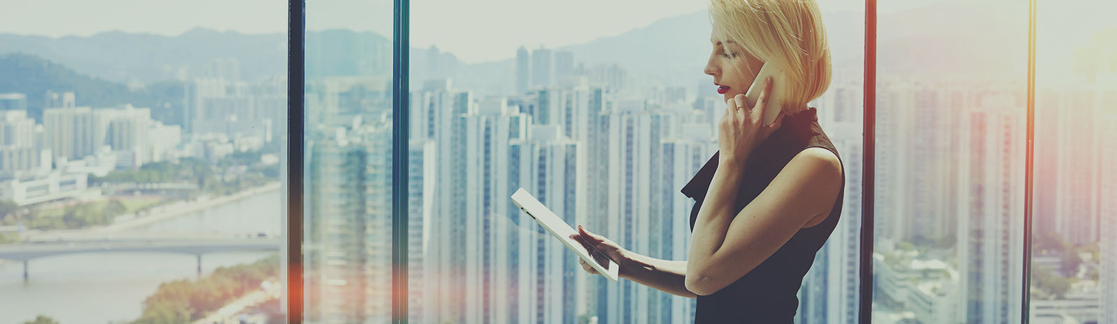 woman holding phone and looking at an ipad at a high rise building